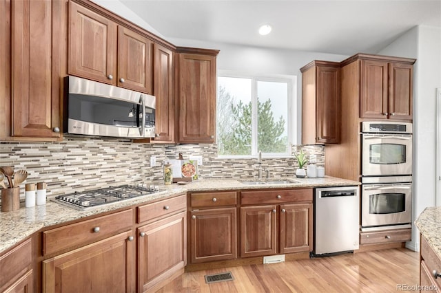 kitchen with appliances with stainless steel finishes, a sink, backsplash, light wood-style floors, and recessed lighting
