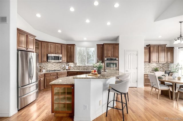 kitchen featuring stainless steel appliances, a kitchen island, decorative backsplash, a sink, and a breakfast bar