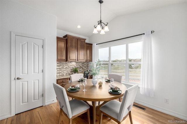 dining room with vaulted ceiling, a chandelier, light wood-style floors, and baseboards