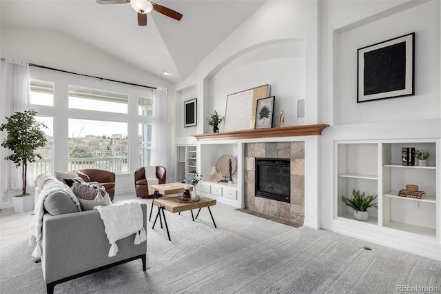 carpeted living area featuring vaulted ceiling, a tiled fireplace, a ceiling fan, and built in shelves