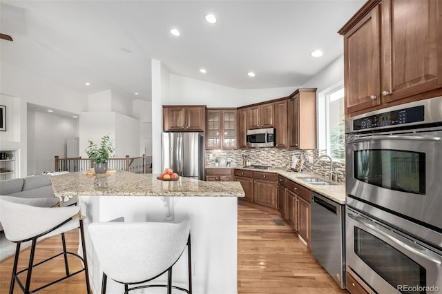 kitchen featuring stainless steel appliances, a sink, lofted ceiling, a kitchen breakfast bar, and decorative backsplash