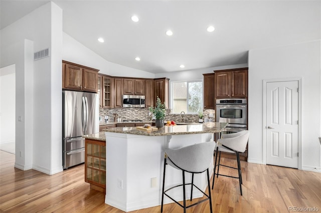 kitchen featuring appliances with stainless steel finishes, tasteful backsplash, a center island, a kitchen breakfast bar, and light stone counters