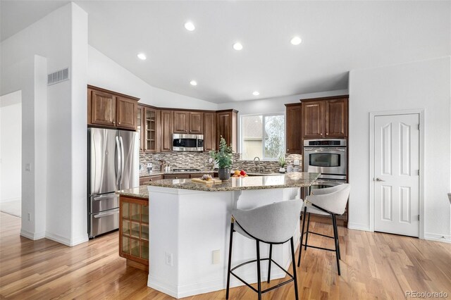 8802 E 148th Ln, Thornton, CO 80602 - kitchen with appliances with stainless steel finishes, tasteful backsplash, a kitchen island, a kitchen breakfast bar, and light stone counters