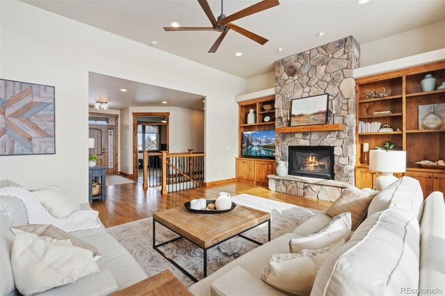 living room with ceiling fan, a stone fireplace, and light wood-type flooring