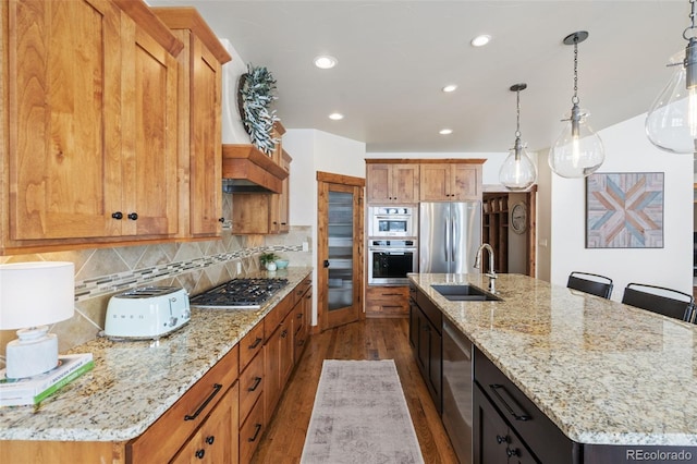 kitchen featuring appliances with stainless steel finishes, sink, decorative light fixtures, and a kitchen island with sink