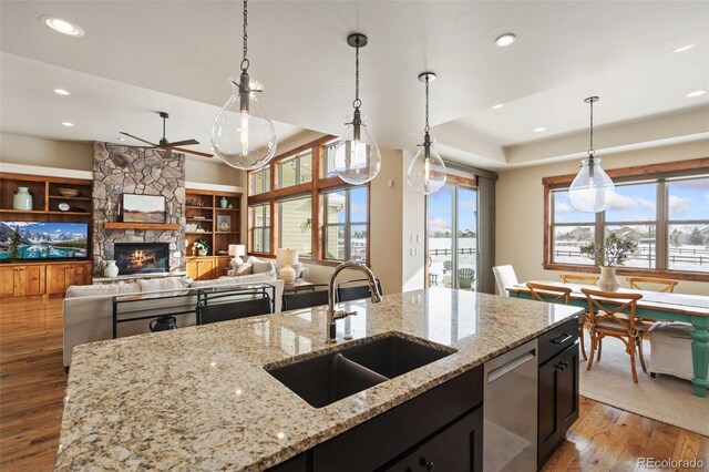 kitchen featuring sink, hanging light fixtures, stainless steel dishwasher, light stone counters, and a tray ceiling