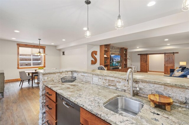 kitchen featuring pendant lighting, sink, dishwasher, light stone countertops, and a barn door