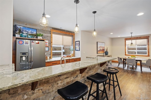 kitchen with stainless steel refrigerator with ice dispenser, a breakfast bar, light stone countertops, and hanging light fixtures