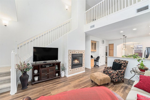 living room with a towering ceiling, hardwood / wood-style flooring, a notable chandelier, and a tiled fireplace