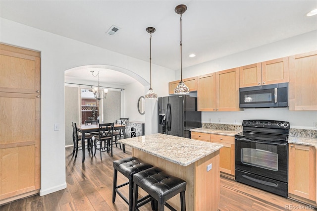 kitchen featuring a breakfast bar, decorative light fixtures, light brown cabinetry, a kitchen island, and black appliances