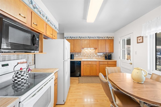 kitchen with tasteful backsplash, light wood-type flooring, light countertops, black appliances, and a sink