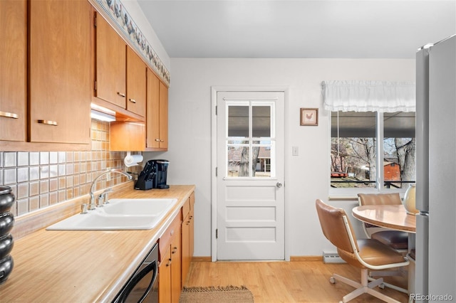 kitchen featuring light wood finished floors, freestanding refrigerator, a sink, light countertops, and backsplash