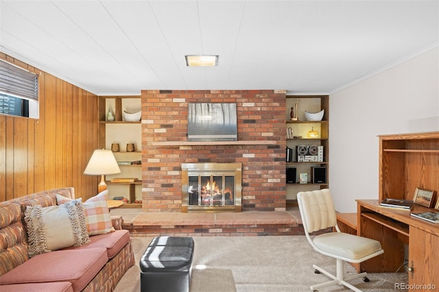 carpeted living room featuring crown molding, a brick fireplace, built in shelves, and wood walls