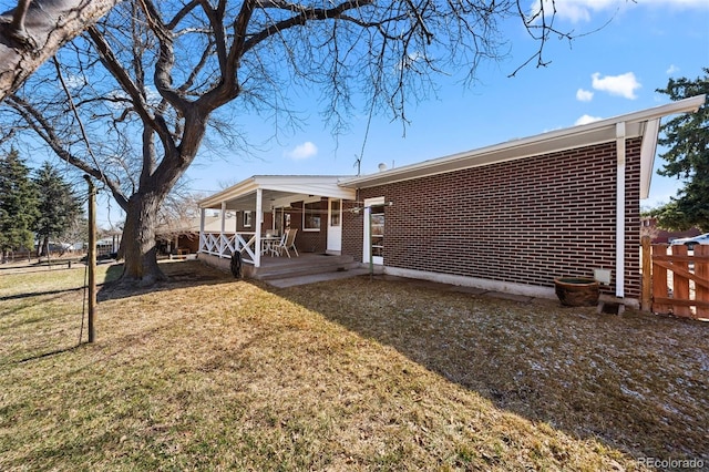 rear view of house with a yard, brick siding, and fence