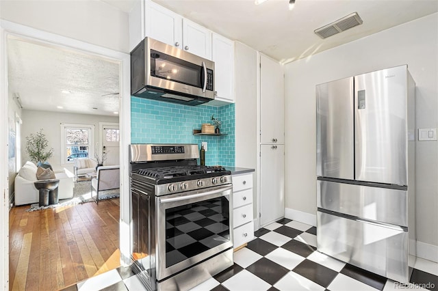 kitchen featuring visible vents, stainless steel appliances, white cabinets, dark floors, and decorative backsplash