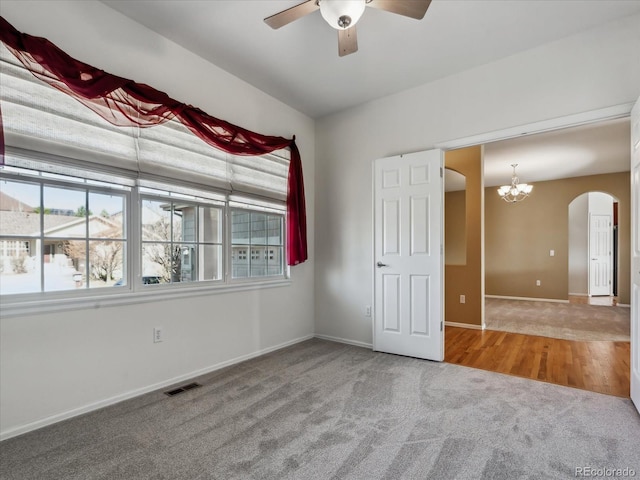 carpeted empty room featuring visible vents, arched walkways, baseboards, and ceiling fan with notable chandelier