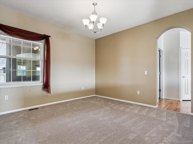 unfurnished room with visible vents, baseboards, carpet, arched walkways, and a notable chandelier