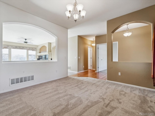 spare room featuring arched walkways, visible vents, ceiling fan with notable chandelier, and carpet floors