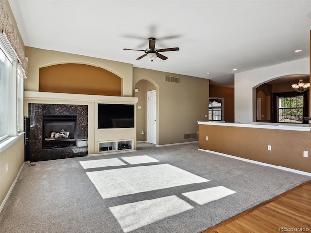 unfurnished living room featuring ceiling fan with notable chandelier, arched walkways, visible vents, and a premium fireplace