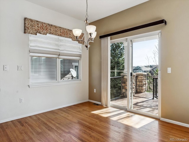 unfurnished dining area with baseboards, wood finished floors, visible vents, and a chandelier