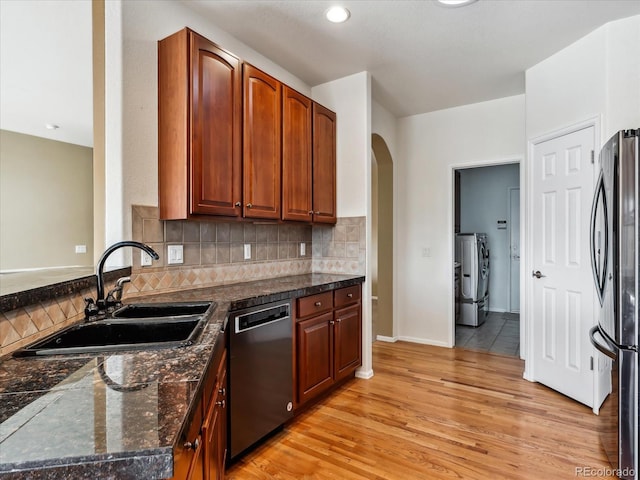 kitchen featuring arched walkways, a sink, stainless steel appliances, light wood-type flooring, and backsplash