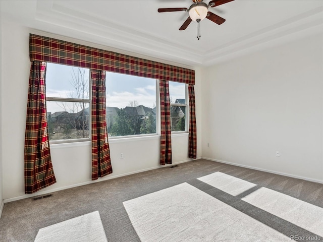 unfurnished room with visible vents, baseboards, ceiling fan, a raised ceiling, and carpet flooring