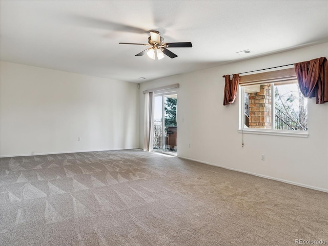 carpeted empty room with a ceiling fan, visible vents, a wealth of natural light, and baseboards