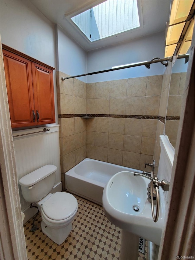 full bathroom with sink, toilet, tiled shower / bath, and a skylight