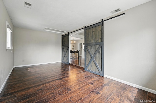 spare room featuring baseboards, visible vents, a barn door, and wood finished floors