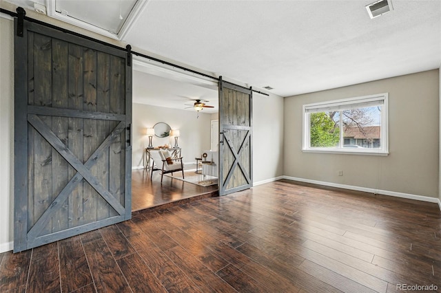 empty room with baseboards, wood finished floors, a barn door, and visible vents