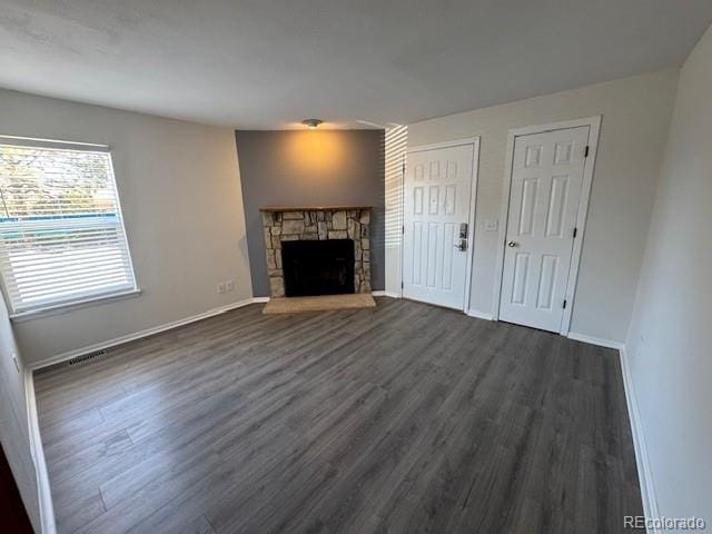 unfurnished living room featuring a stone fireplace, baseboards, dark wood-type flooring, and visible vents