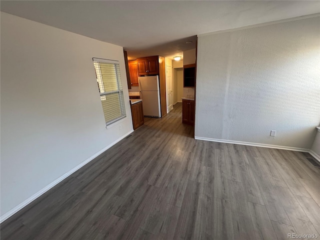 unfurnished living room featuring visible vents, baseboards, and dark wood finished floors