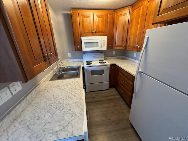 kitchen featuring brown cabinetry, a sink, a textured ceiling, wood finished floors, and white appliances