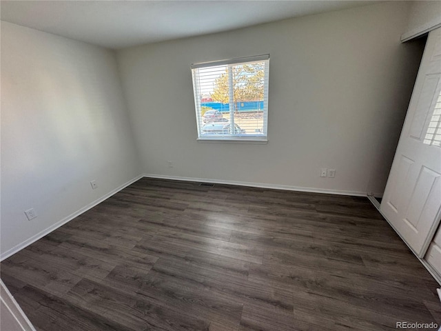 empty room with dark wood-type flooring and baseboards