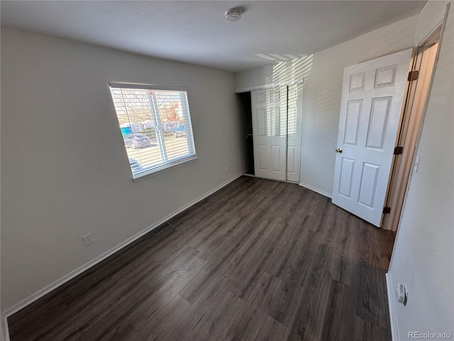 unfurnished bedroom featuring dark wood-style floors, a closet, visible vents, and baseboards