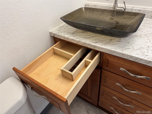 interior details with a textured wall, vanity, and toilet