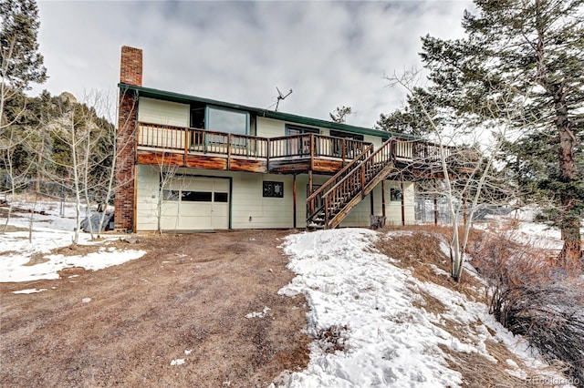 snow covered back of property featuring a garage and a deck