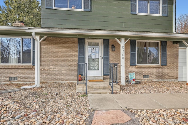 view of exterior entry with crawl space, brick siding, and covered porch