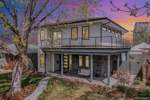 back house at dusk featuring a lawn, a patio area, and a balcony