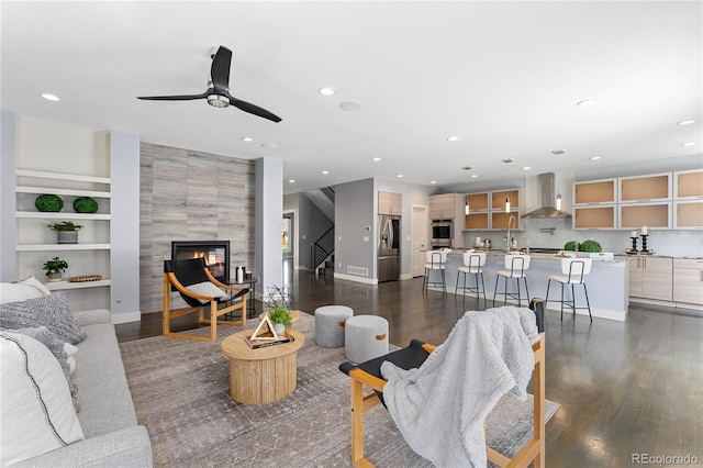 living room featuring a fireplace, built in shelves, ceiling fan, and dark wood-type flooring