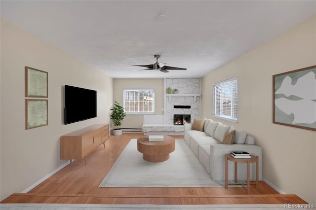 living room featuring ceiling fan, plenty of natural light, a premium fireplace, and light wood finished floors