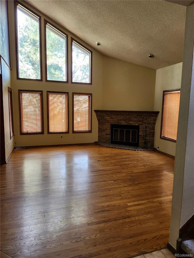 unfurnished living room featuring a brick fireplace, a textured ceiling, vaulted ceiling, and wood finished floors