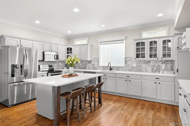 kitchen with ornamental molding, appliances with stainless steel finishes, a sink, and a breakfast bar area