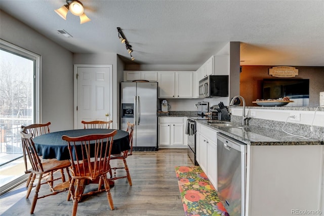 kitchen with a sink, dark stone countertops, white cabinetry, stainless steel appliances, and a peninsula