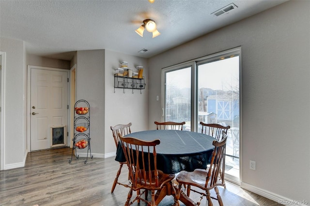 dining area featuring visible vents, a textured ceiling, baseboards, and wood finished floors