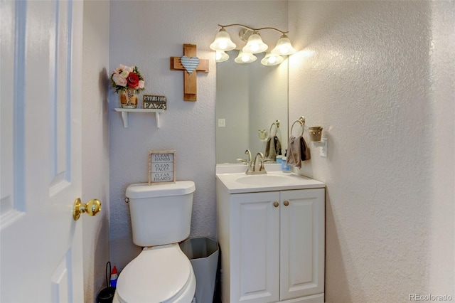 bathroom featuring toilet, vanity, and a textured wall