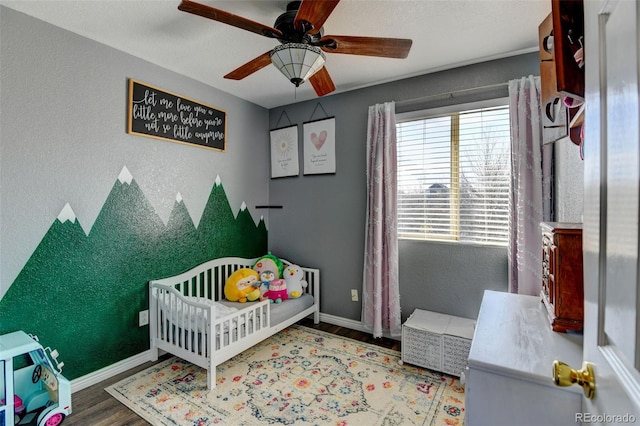 bedroom with a textured wall, baseboards, a nursery area, and wood finished floors