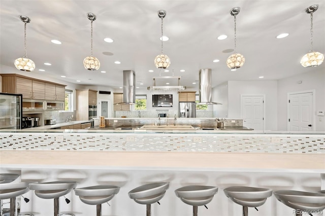 kitchen featuring pendant lighting, island range hood, appliances with stainless steel finishes, and tasteful backsplash