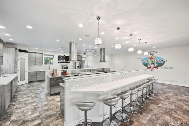 kitchen featuring gray cabinets, hanging light fixtures, wall chimney range hood, and island exhaust hood