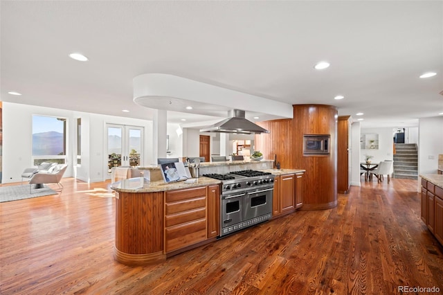 kitchen featuring light stone countertops, range with two ovens, island exhaust hood, and dark hardwood / wood-style floors